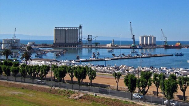 A coastal industrial area with large storage tanks, a marina with boats, and a beach with parked cars. - B&B Charming House (Barletta)