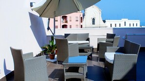 A rooftop terrace with wicker furniture, an umbrella, and a view of a building with a dome and balconies. - B&B Charming House (Barletta)