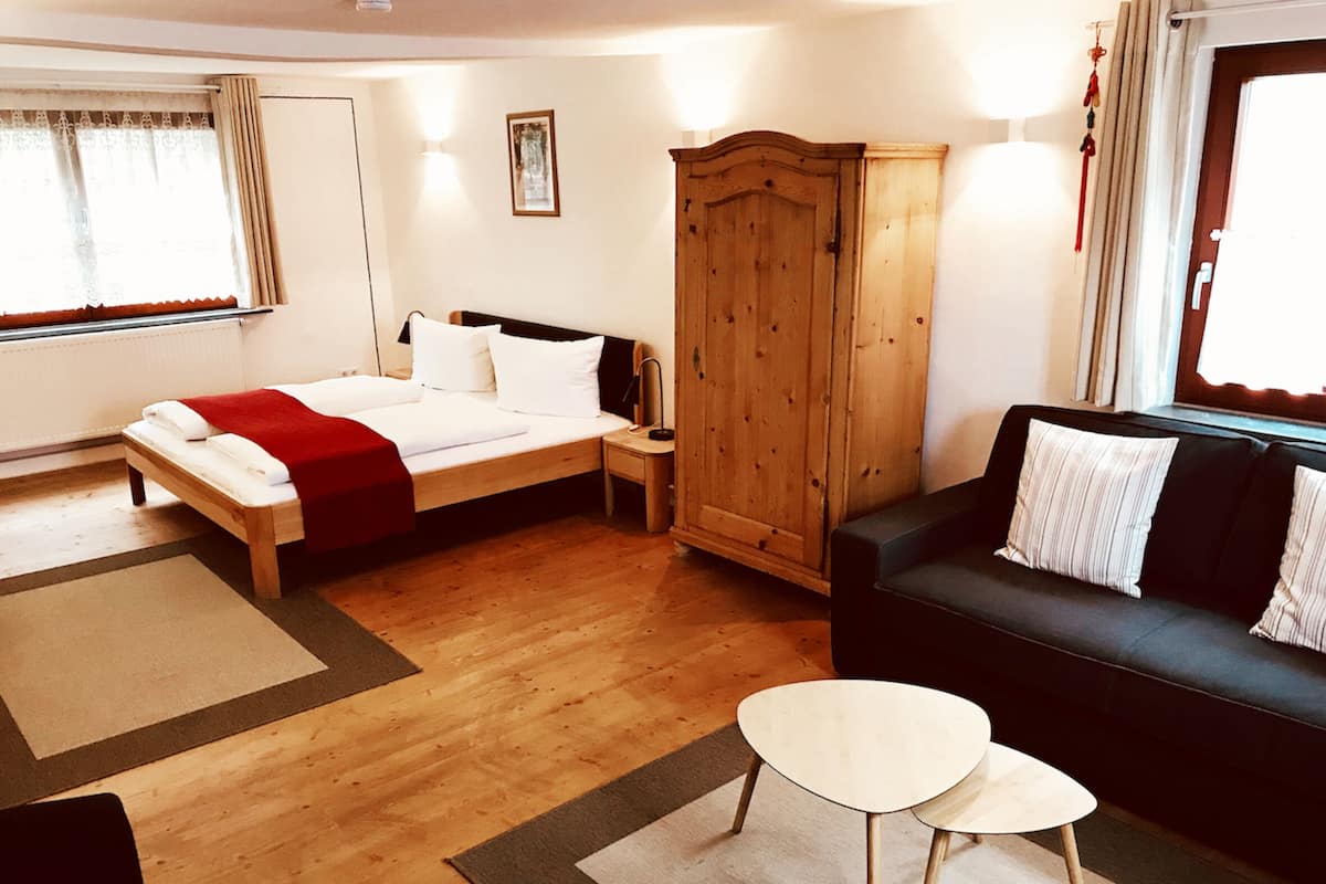 Ein Hotelzimmer mit Bett, Sofa, kleinem Tisch, Schrank und einem Fenster mit Vorhängen.