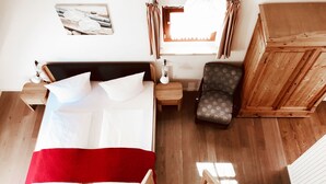 Een slaapkamer met een bed, een stoel, een nachtkastje en een houten garderobe.