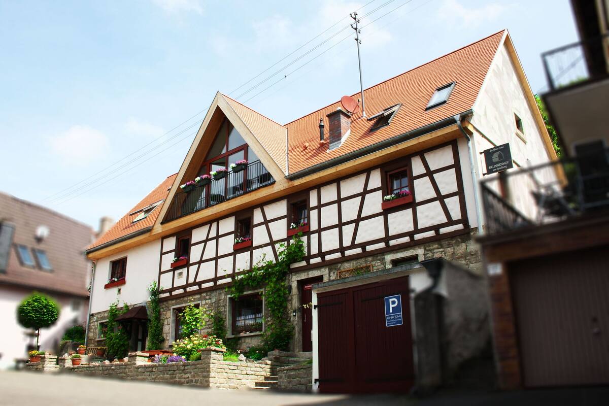 Ein traditionelles Fachwerkhäuschen mit rotem Ziegeldach, einem Balkon mit Blumentöpfen und einem Parkplatzschild.
