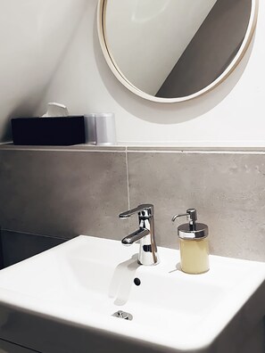 A bathroom with a white sink, a round mirror, and a soap dispenser. - Brunnenhof Randersacker - Das Kleine Hotel (Randersacker)
