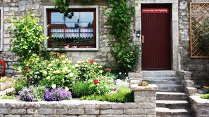 Een stenen gebouw met een rode deur, een raam met een witte gordijn, en een tuin met verschillende bloemen.