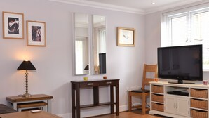 A living room with a wooden floor, a TV, a desk, a chair, a lamp, and framed pictures on the wall. - Stagedoor Apartment (Eastbourne)