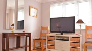 A living room with a flat-screen TV, wooden furniture, wicker baskets, and a window with blinds. - Stagedoor Apartment (Eastbourne)