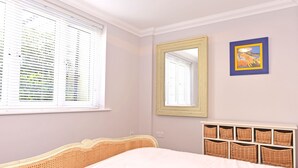 A bedroom with a bed, a window with blinds, a mirror, and a wall-mounted basket storage unit. - Stagedoor Apartment (Eastbourne)
