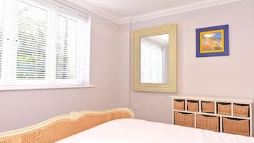 Quarto com cama, janela com persianas, espelho e unidade de armazenamento em cesta fixada na parede.