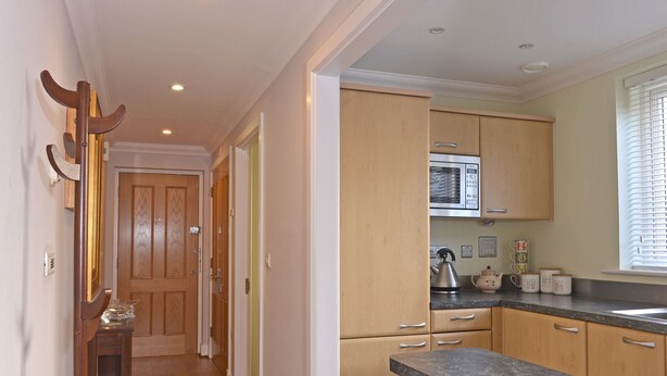 A kitchen with wooden cabinets, a stainless steel refrigerator, and a countertop. - Stagedoor Apartment (Eastbourne)