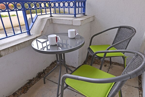 Een klein buiten zitgedeelte met een ronde tafel en twee stoelen, waarvan één met een groene kussen.