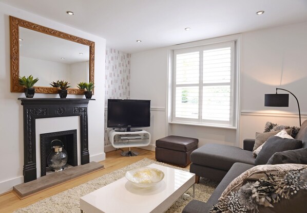 A modern living room with a fireplace, a television, a sofa, and a large window. - Urban Chic (Eastbourne)