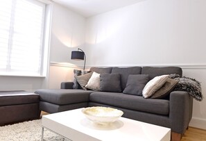 A modern living room with a grey sectional sofa, a white coffee table, and a black floor lamp. - Urban Chic (Eastbourne)