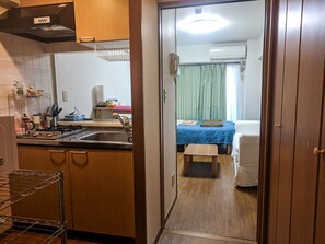 A compact kitchen with a sink, stove, and storage shelves. A small dining table is visible in the adjacent room.