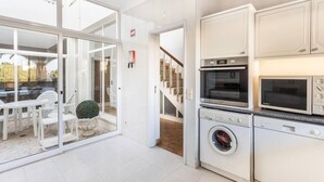 A modern kitchen with built-in appliances, a dining area with a glass door leading to an outdoor patio, and a staircase connecting to another level. - Casa da Ermida near the beach and golf course (Budens)
