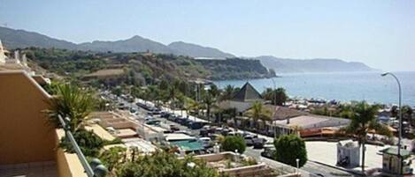 A coastal hotel with a pool area, a view of the sea, and a parking lot.