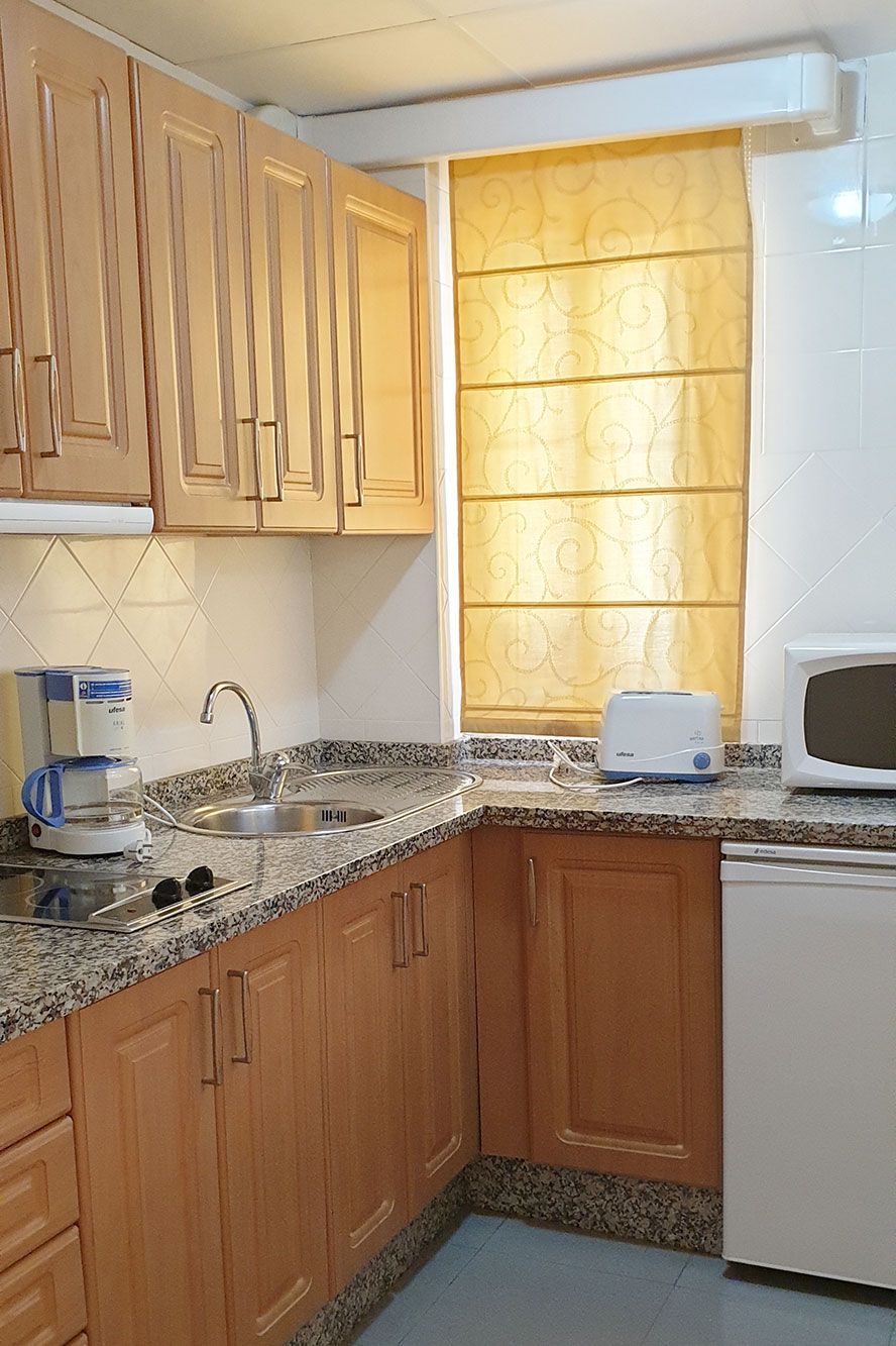 Una cocina con gabinetes de madera, una encimera de granito, un tostador, un microondas y una ventana con cortina estampada.