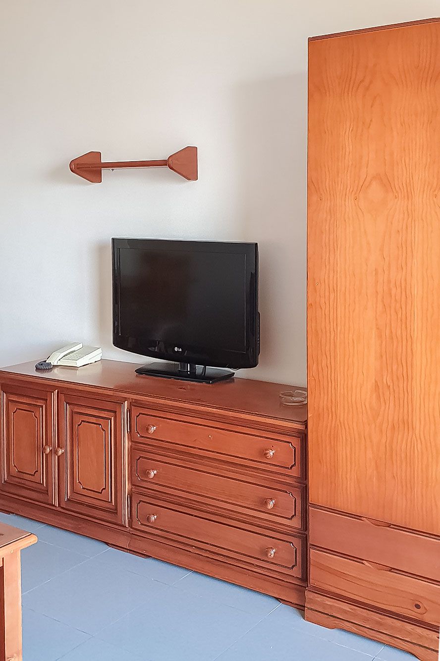 A television on a wooden cabinet with drawers, a book, and a remote control.