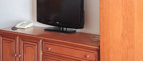 A television on a wooden cabinet with drawers, a book, and a remote control.