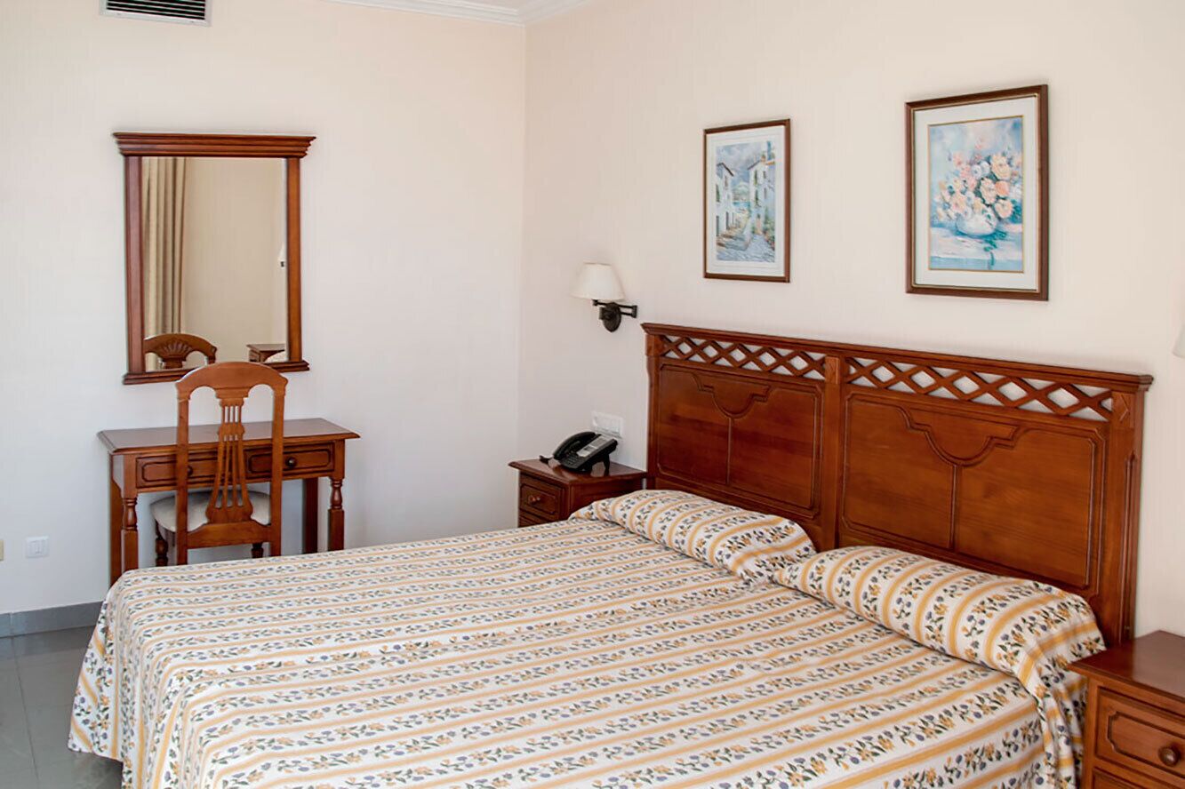 Ein Schlafzimmer mit einem Holzbett, einem Schreibtisch, einem Stuhl und zwei gerahmten Bildern an der Wand.
