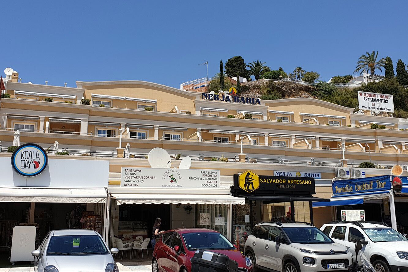 Un hotel de varios pisos, con terraza exterior y diversas tiendas, incluyendo una zapatería y un bar de cócteles.
