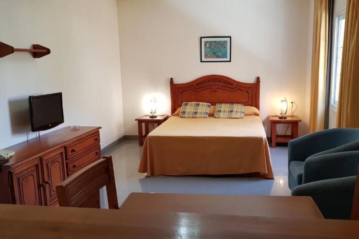 A hotel room with a bed, a desk, a chair, a television, and two bedside lamps.
