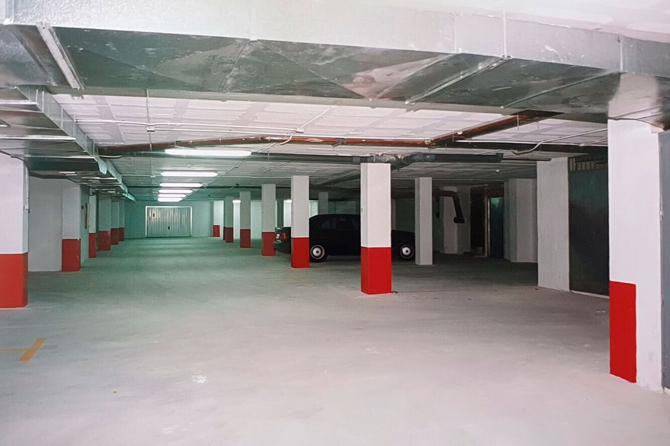 A parking garage with concrete pillars and a car parked in one of the spaces.