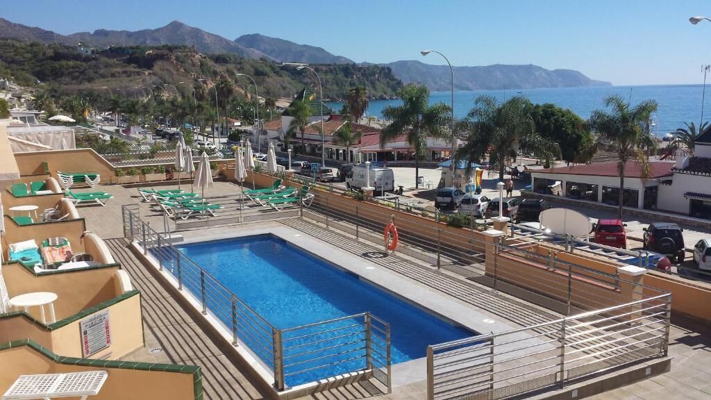 Une piscine sur le toit, agrémentée de chaises longues et de parasols, entourée d’immeubles et offrant une vue sur la mer.