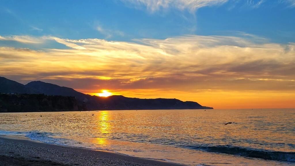 Ein Sonnenuntergang über einem ruhigen Meer, im Hintergrund ein fernes Gebirge.