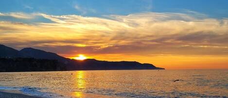 Ein Sonnenuntergang über einem ruhigen Meer, im Hintergrund ein fernes Gebirge.