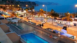 A rooftop pool area with a view of the sea, surrounded by palm trees and street lights. - Nerja Bahía Apartamentos (Nerja)