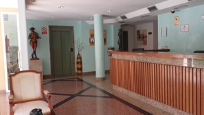 A reception area with a wooden reception desk, a chair, a statue, and a door. - Nerja Bahía Apartamentos (Nerja)