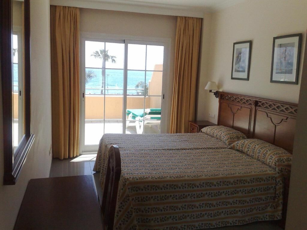 Ein Hotelzimmer mit zwei Betten, Meerblick durch eine Schiebetür und einem Balkon mit Tisch und Stühlen.