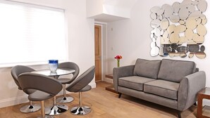 Una sala de estar moderna con un sofá gris, dos sillas grises, una mesita redonda y una pared decorativa con espejos.