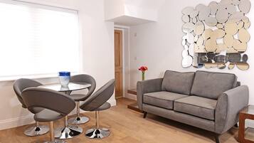 Uma sala de estar moderna com um sofá cinzento, duas poltronas cinzentas, uma mesa redonda pequena e uma parede decorativa com espelhos.