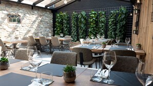An outdoor dining area with stone walls, wooden tables, and chairs. - Hotel Restaurant Inn Naeldwyk (Naaldwijk)