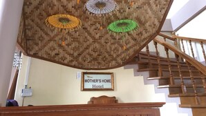 Un escalier avec une rampe en bois et un plafond en osier orné de parapluies suspendus. Une enseigne indique : « Hôtel MOTHER'S HOME ».