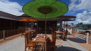 Un espace extérieur aménagé pour les repas, avec des tables et des chaises, un parasol vert et une vue sur les bâtiments en arrière-plan.