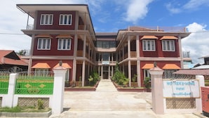 Un hôtel de deux étages avec une entrée principale, une enseigne et une allée d’accès fermée par un portail.