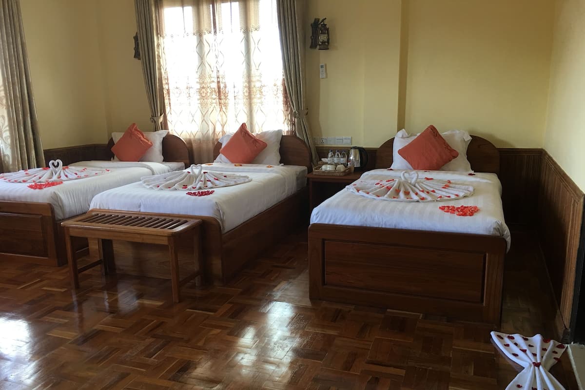 A hotel room with three wooden beds, each with a white bedspread and red heart-shaped decorations. There is a wooden bench in the center, and a small table with a kettle and cups on the side.