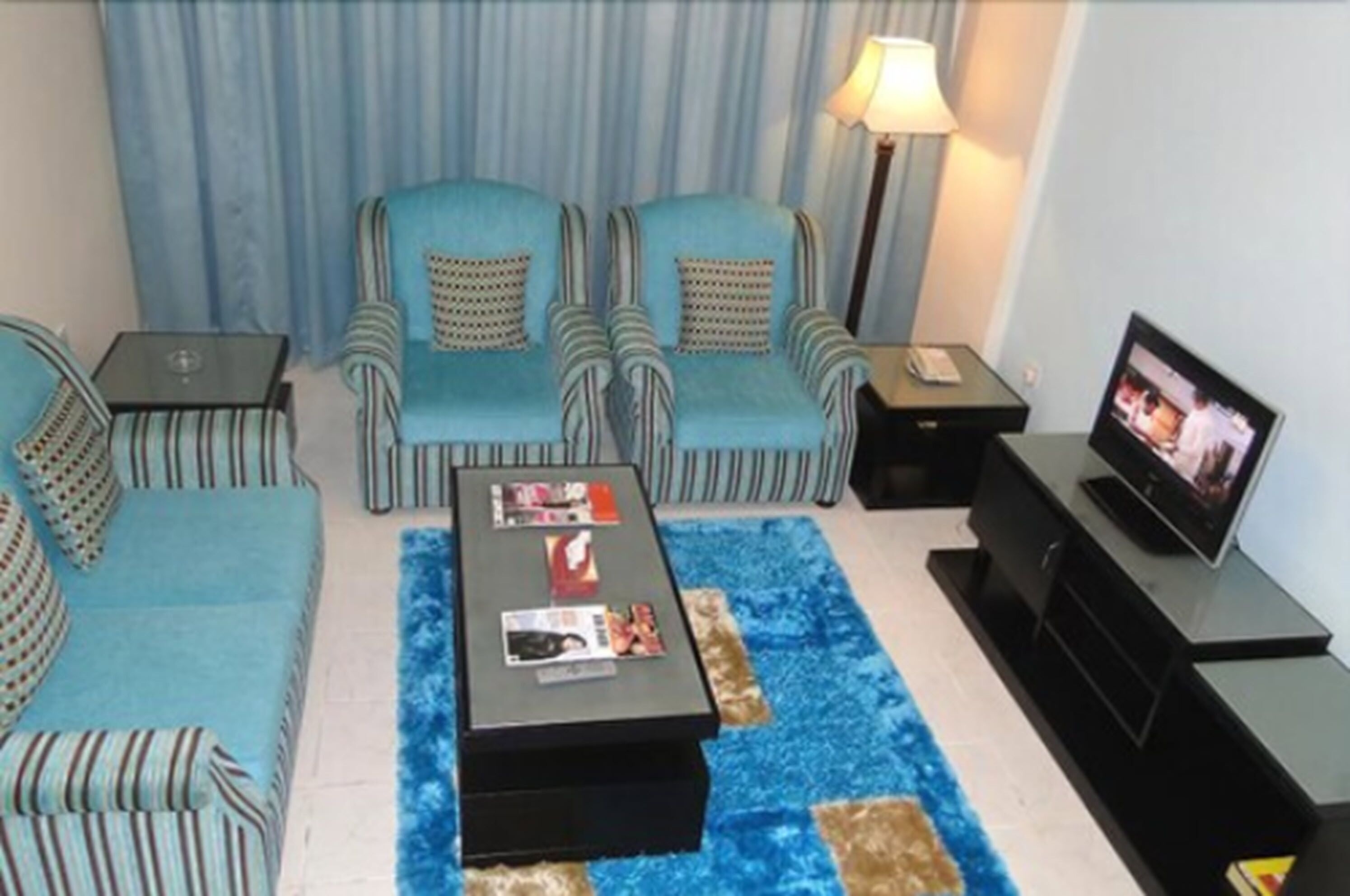 A living room with two striped sofas, a coffee table with magazines, a TV on a stand, and a lamp.