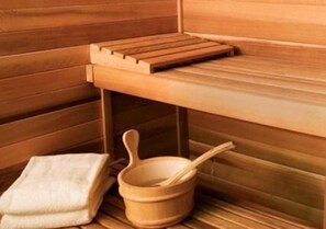 A wooden sauna with a bench, a small table, and a bucket with a ladle. - Al Jazeera Hotel Apartments LLC (Dubai)