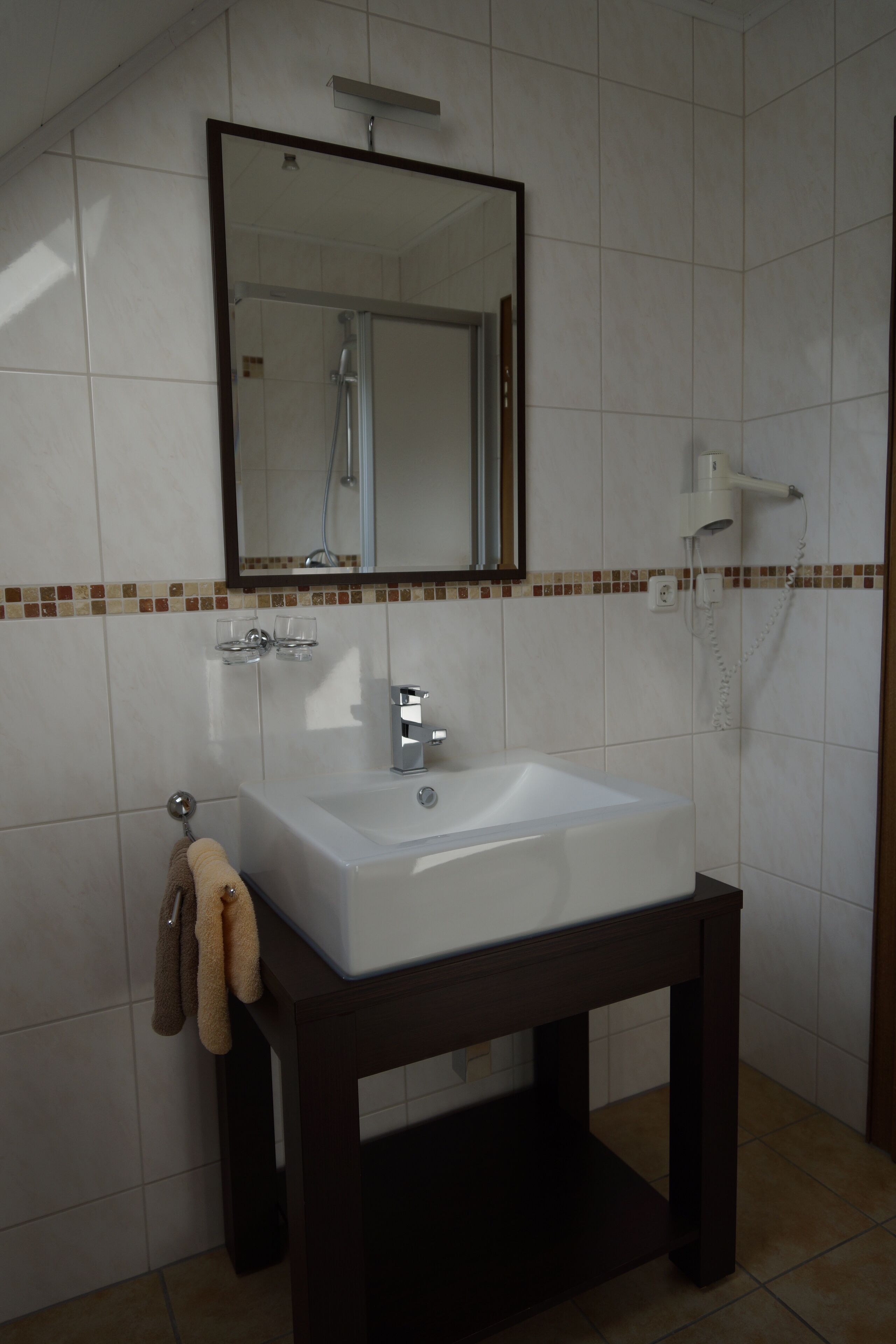 Un baño con lavamanos blanco, un espejo encima y un cabezal de ducha.