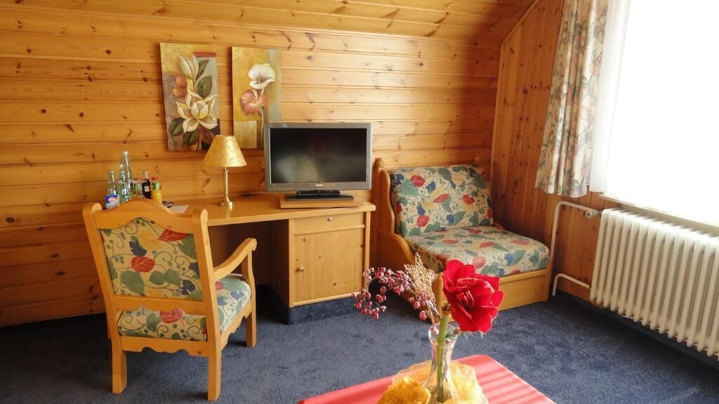 A cozy room with a wooden desk, a television, a floral chair, and a small sofa.