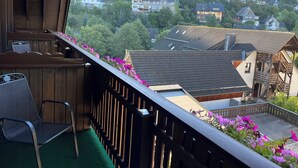A balcony with wooden railings, a chair, and a view of houses and trees. - Landgasthof Göbel (Willingen)
