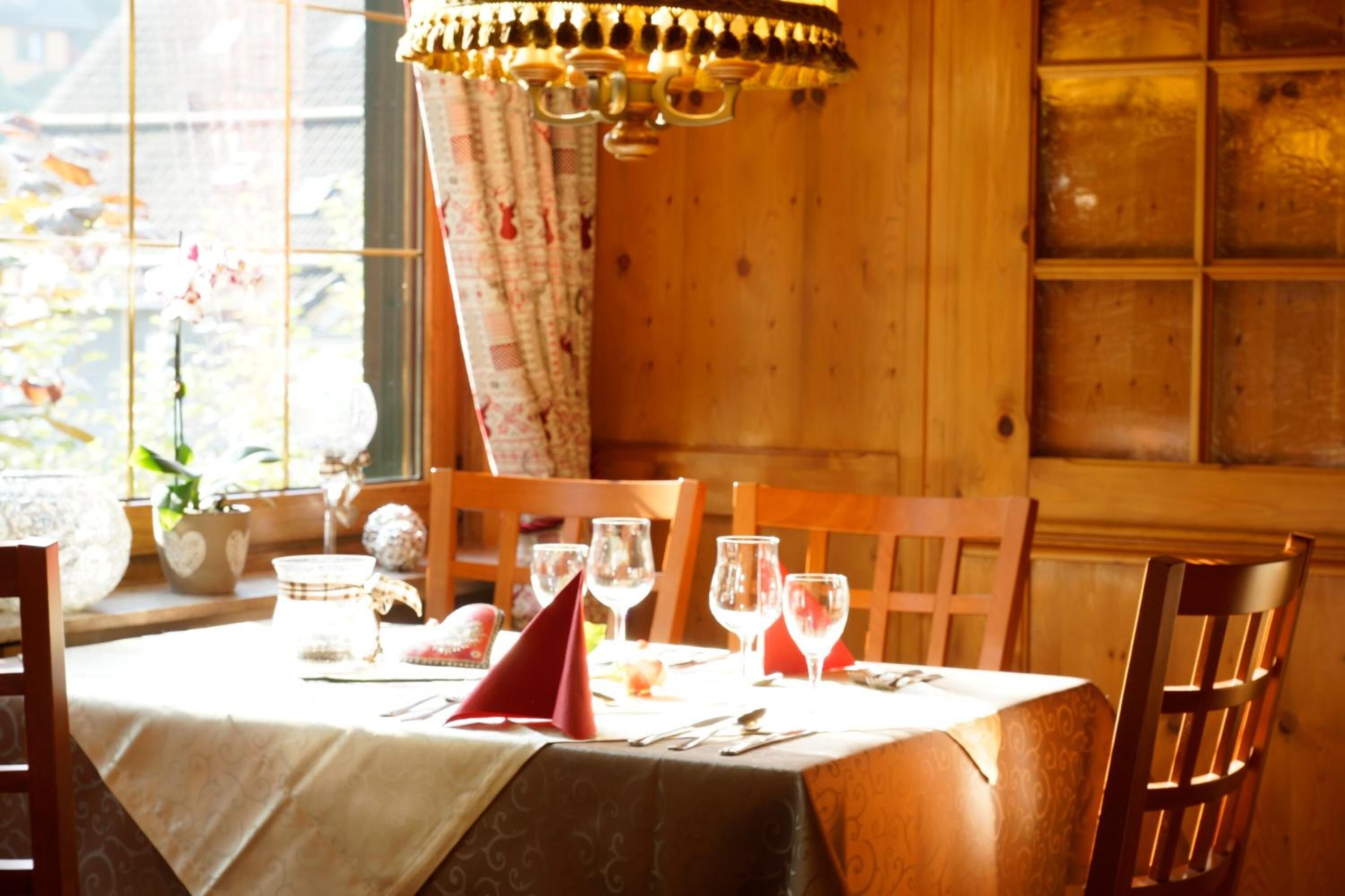 A dining table set with wine glasses, plates, and cutlery, a red napkin, and a chandelier.