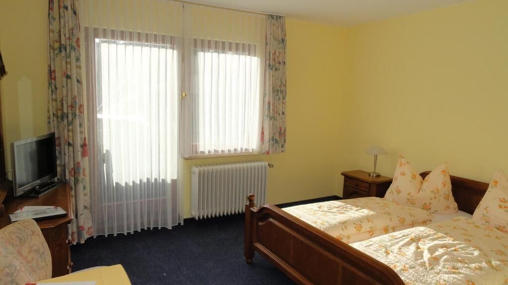 A bedroom with a bed, a television, a radiator, and curtains.