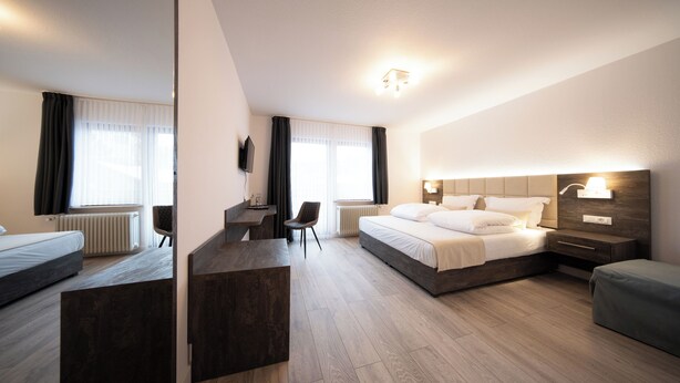 A modern hotel room with a large bed, a desk, and a seating area. - Landgasthof Göbel (Willingen)
