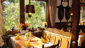 A dining area with a table set for four, a window with a view of greenery, and a hanging light fixture. - Landgasthof Göbel (Willingen)