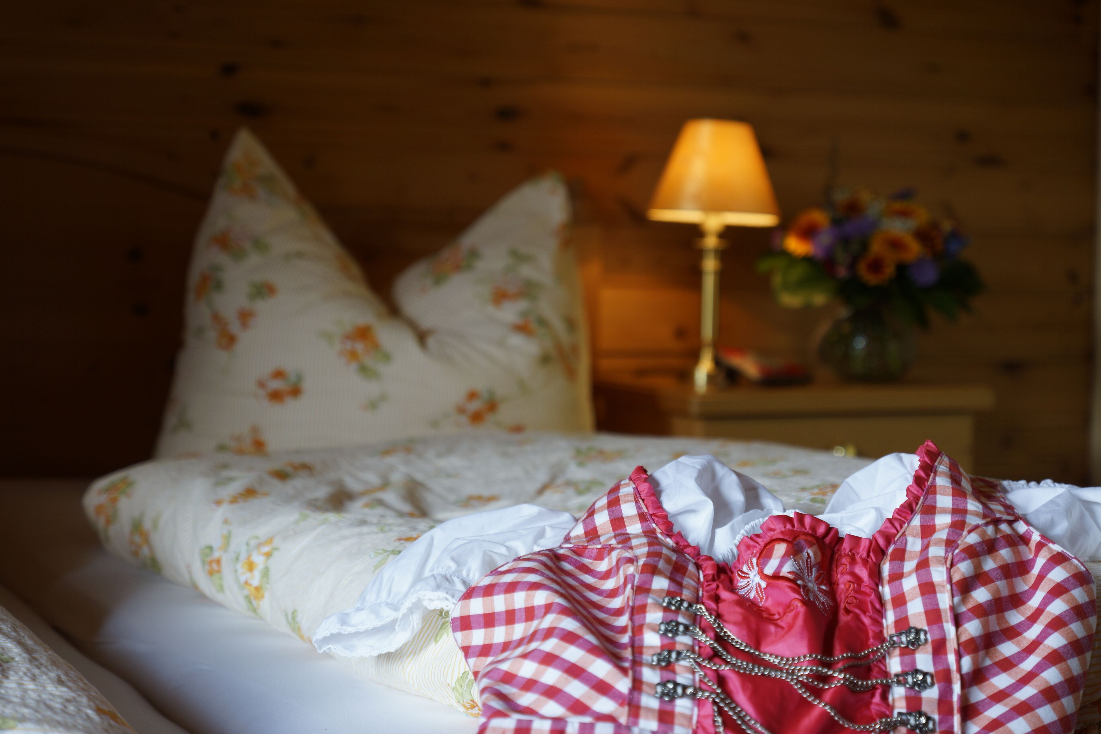 Una cama bien hecha con almohadillas florales, una lámpara de noche y un jarrón con flores.