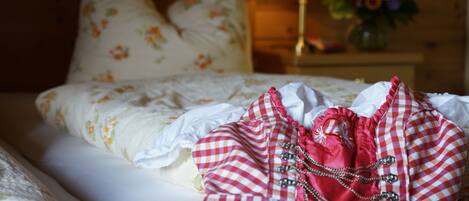 Una cama bien hecha con almohadillas florales, una lámpara de noche y un jarrón con flores.