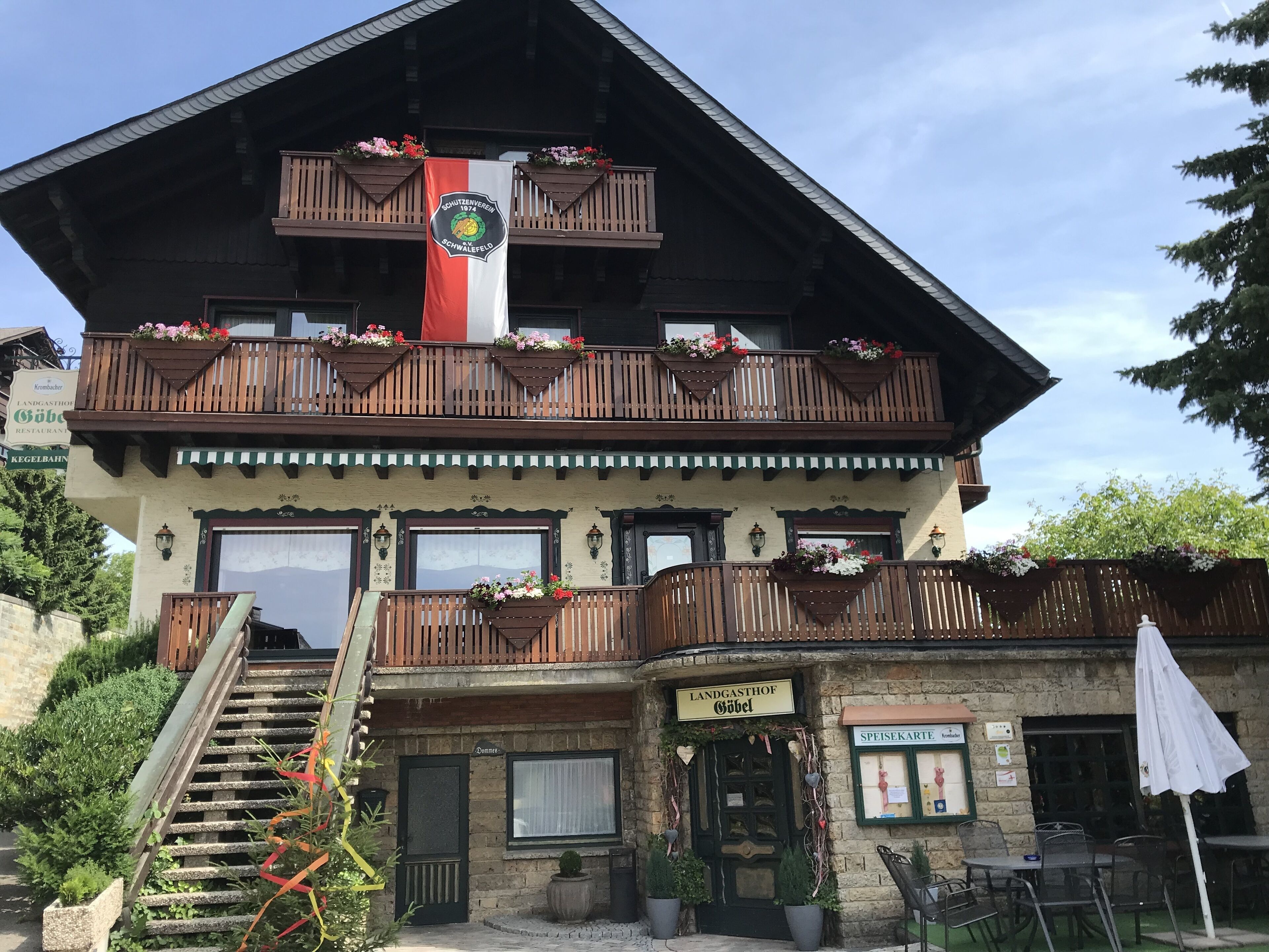 A traditional alpine building with a wooden balcony, a flag, and a sign indicating it's a restaurant.